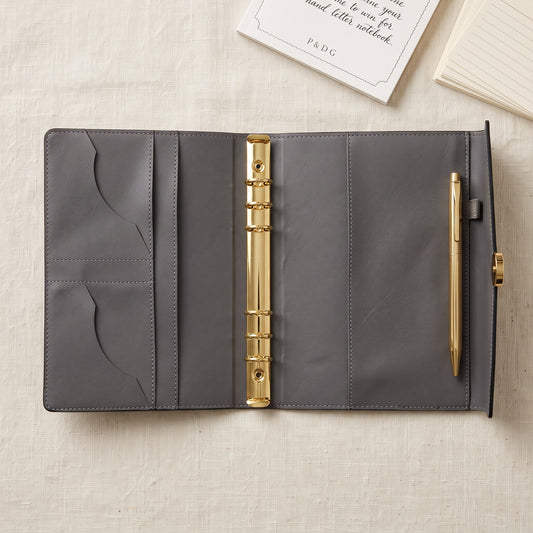 Open Noir A5 binder showing the six-ring gold mechanism and functional interior storage pockets.
